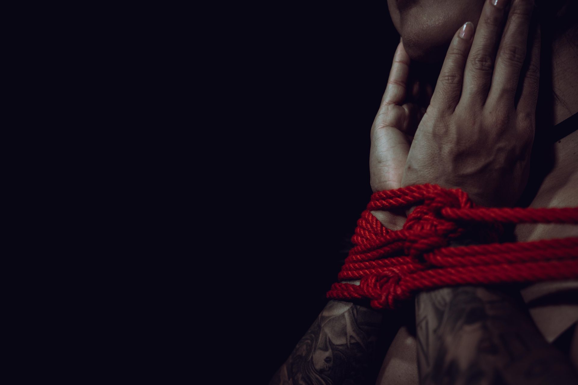 Red rope tied around a person's wrist; hand raised to face. Dark background.