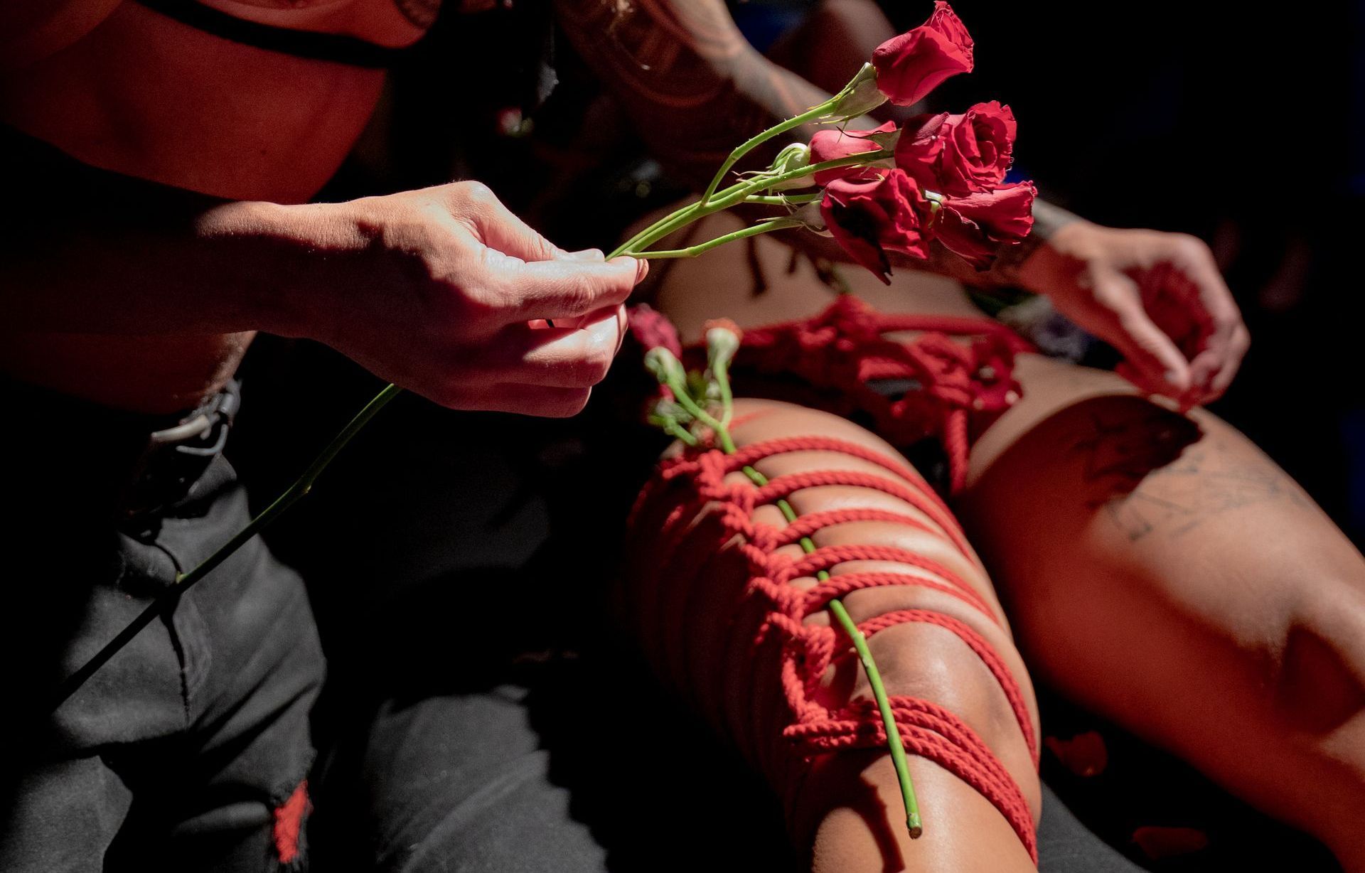 Person tying red rope around leg, holding red roses.