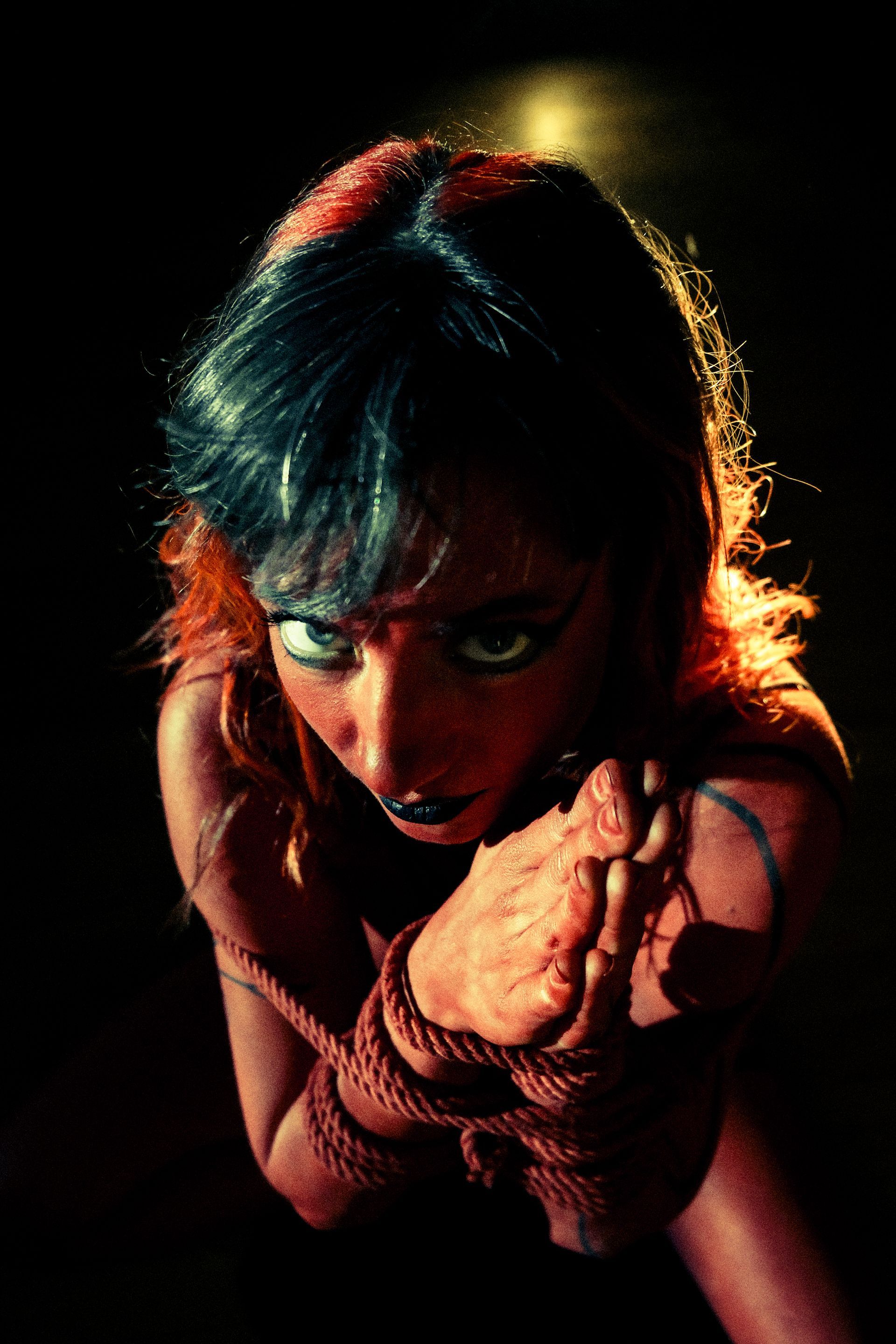 Woman, bound hands, looking up, dramatic lighting.