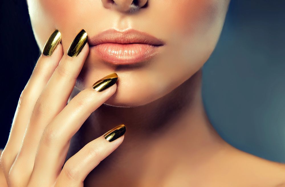 La mano de una persona, con las uñas pintadas en color dorado metalizado, descansa cerca de su barbilla