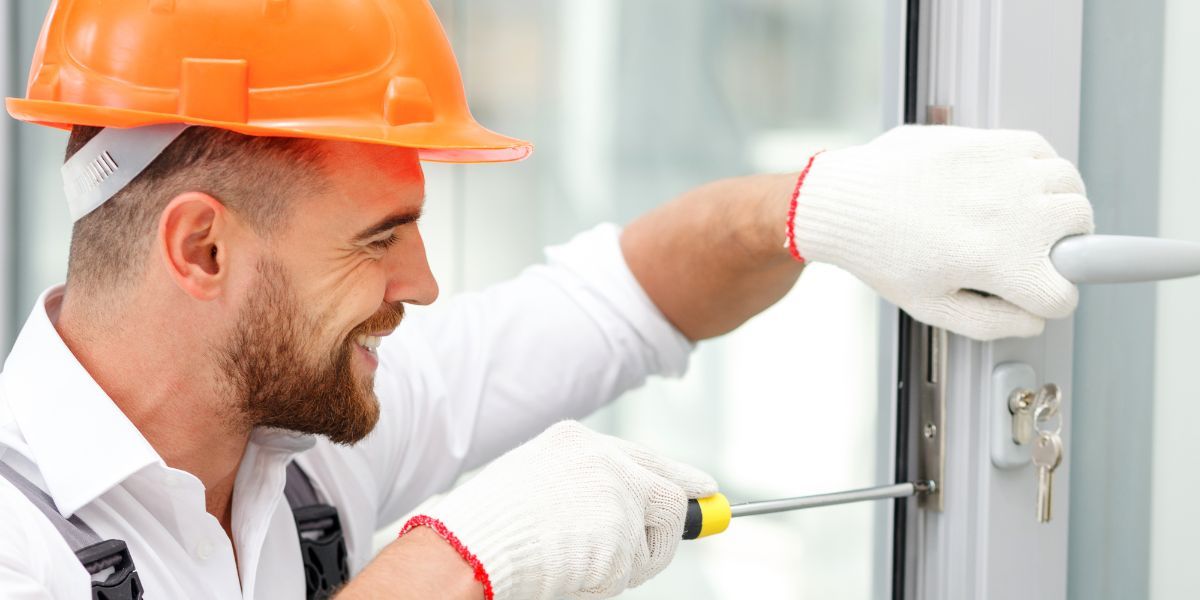 Replacing Locks — Concord, NC — A A L Lock & Key A man with an orange hard hat and gloves smiling while fixing a door lock.
