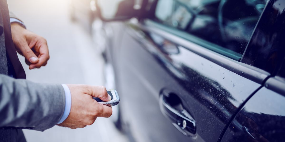 Key Fob Batteries — Concord, NC — A A L Lock & Key A person in a suit unlocks a black car with a key fob outdoors.