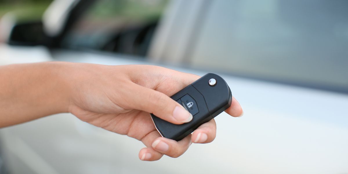 Car Remote Key — Concord, NC — A A L Lock & Key Person's hand holding a black car key fob near a silver car door.