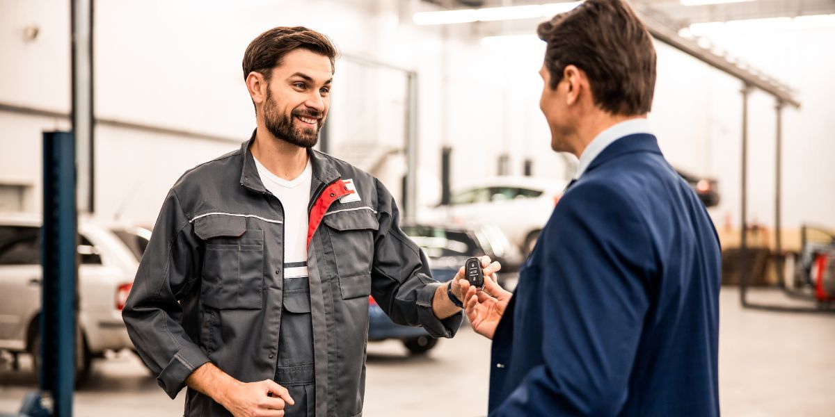 Remote Starter — Concord, NC — A A L Lock & Key Mechanic hands car keys to a man in a suit, in an auto repair shop.