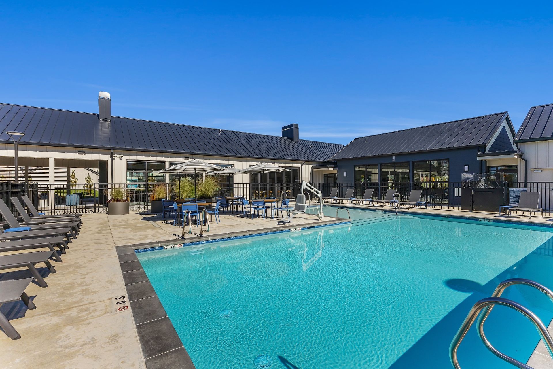Outdoor resort pool with blue water, lounge chairs, and a clubhouse under a clear sky