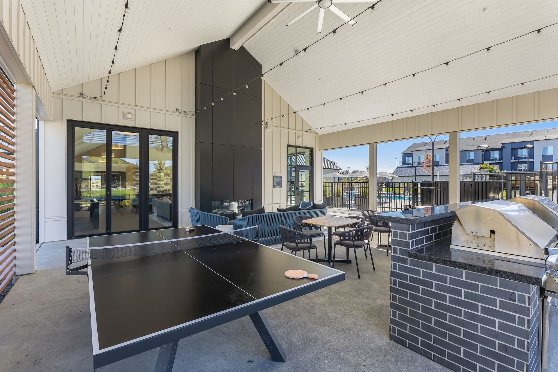 Covered outdoor patio with tables, black brick planters, and lounge seating beside glass doors