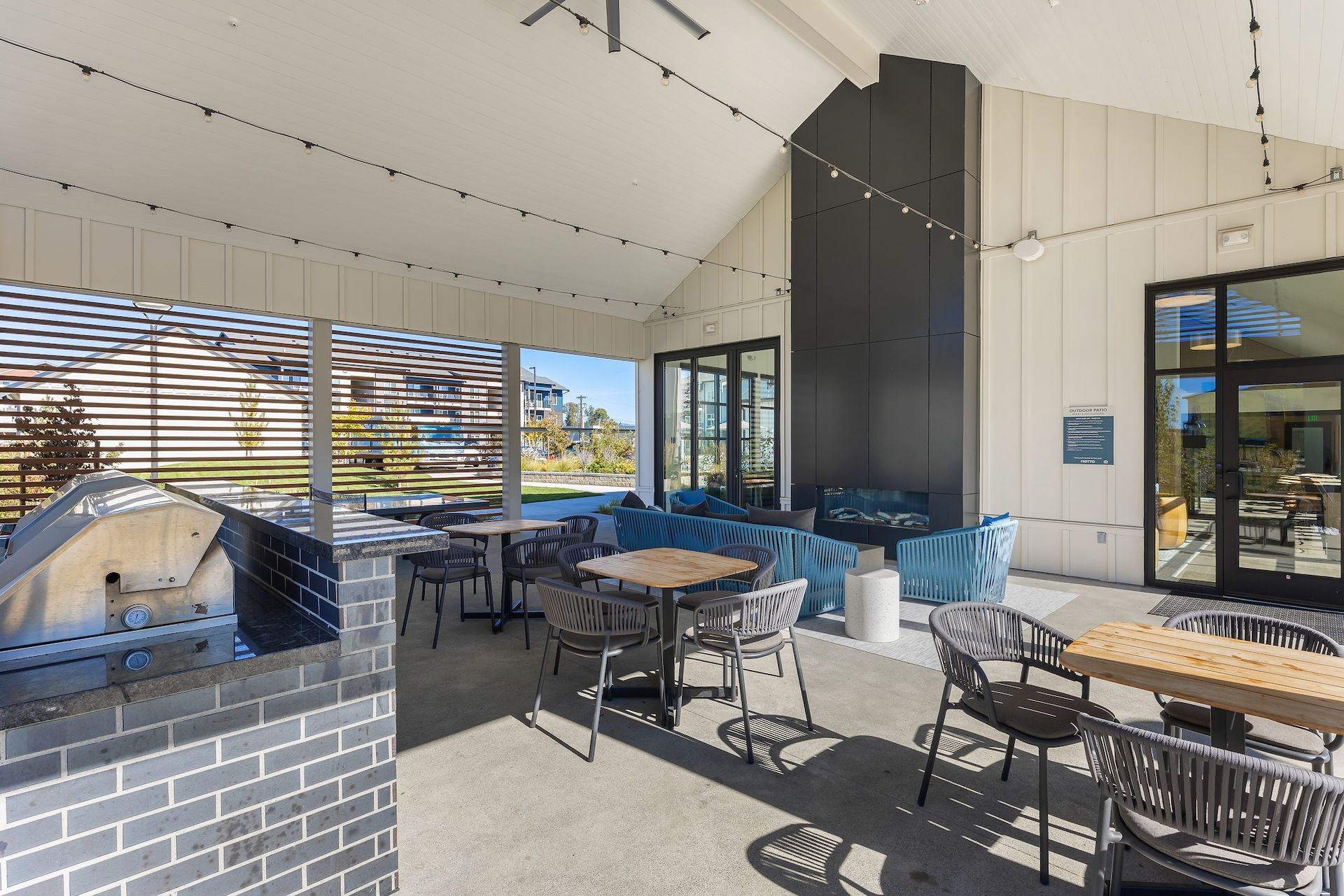 Outdoor patio dining area with tables, chairs, brick grill, and retractable awning in bright sunlight