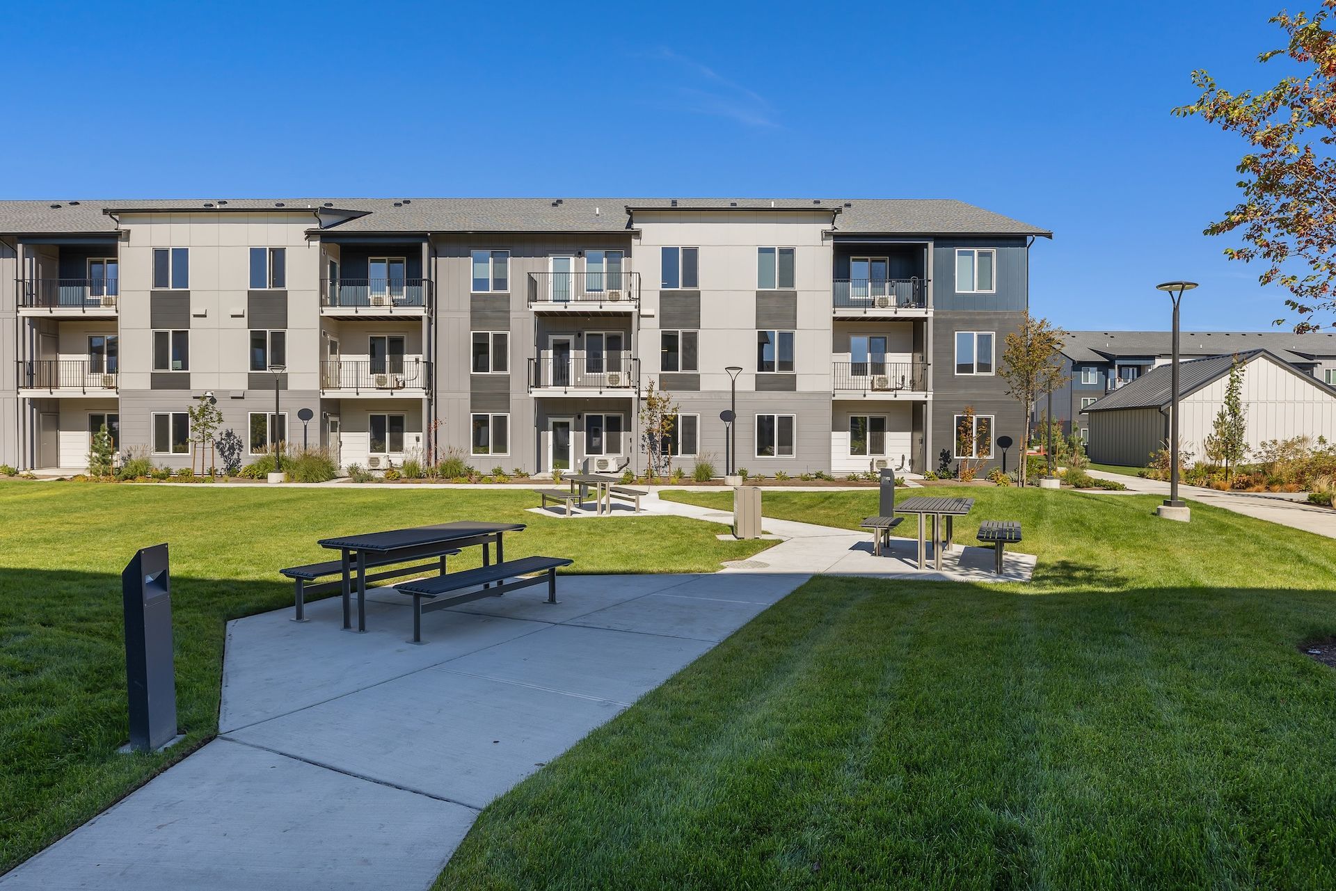 Modern apartment complex with a landscaped courtyard, walkway, benches, and green lawn under a blue sky
