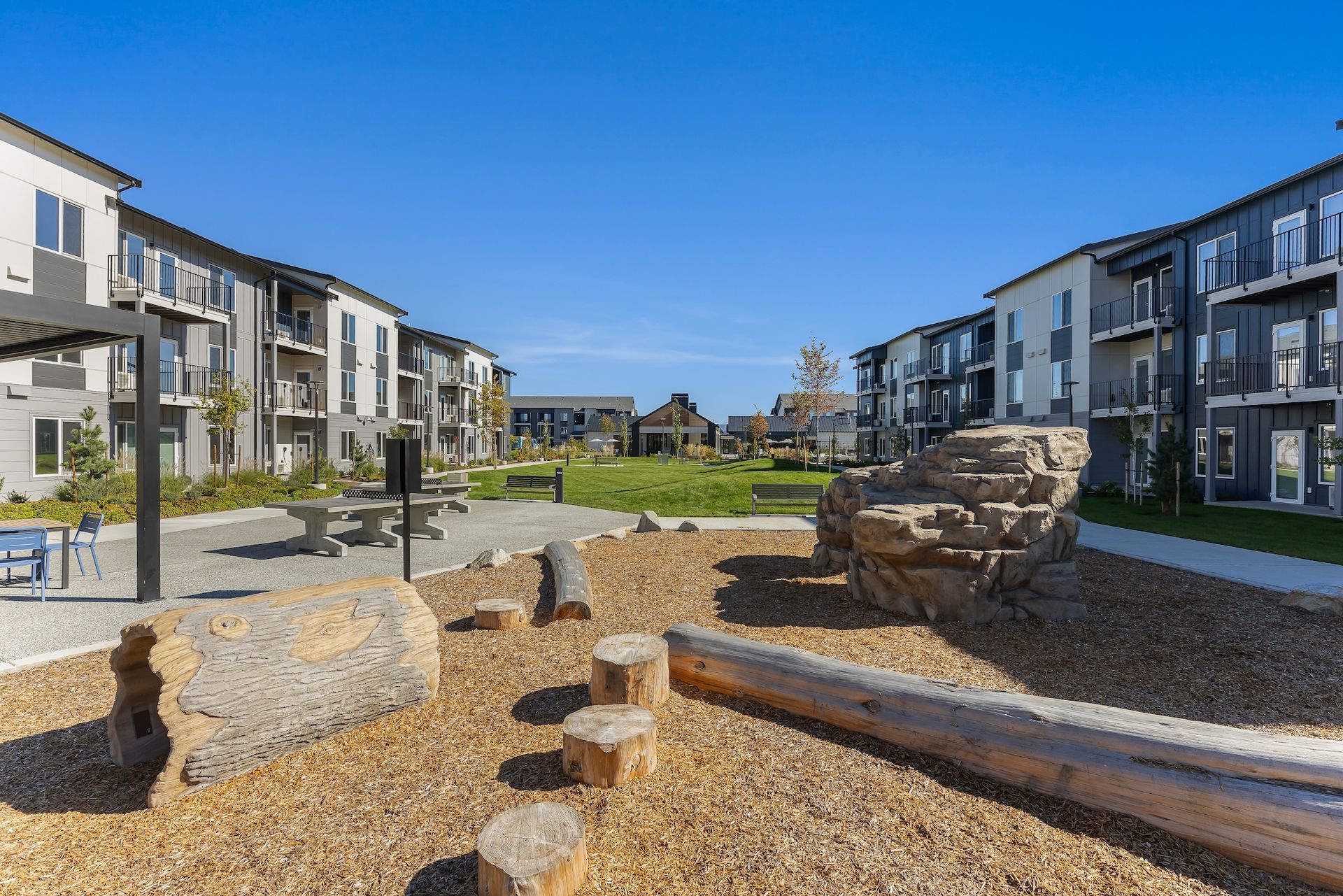 Modern apartment courtyard with gravel paths, benches, and landscaped seating areas under a blue sky