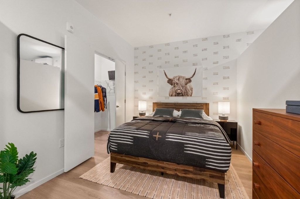A bedroom with a large bed , dresser , and mirror.