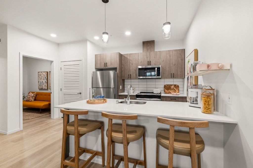 A kitchen with a large island , stools , a refrigerator and a microwave.