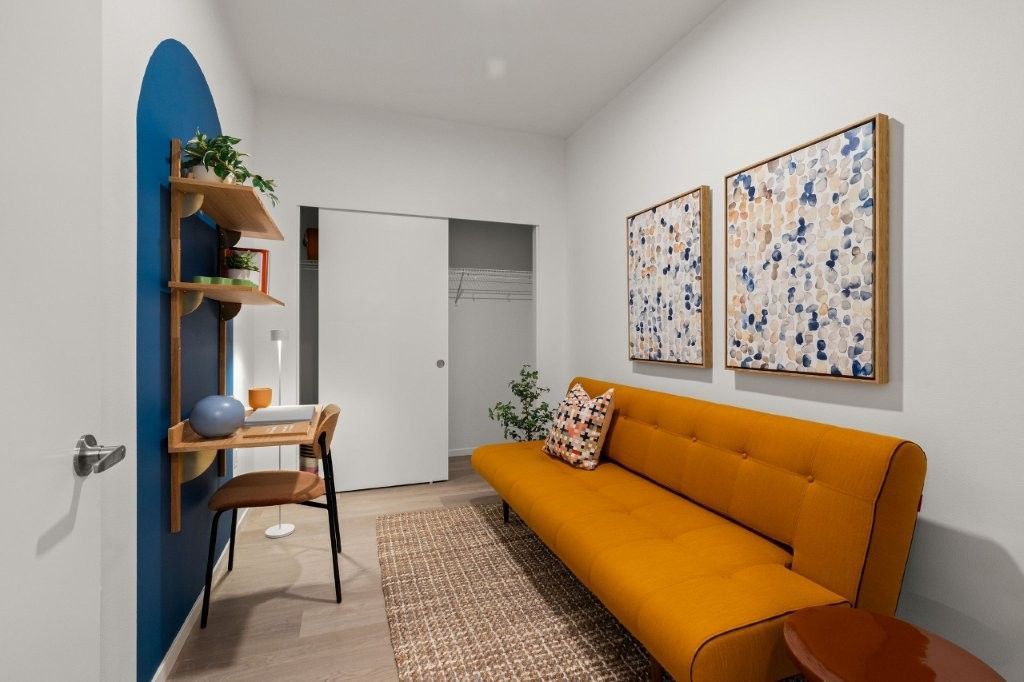 A living room with a yellow couch and a desk.