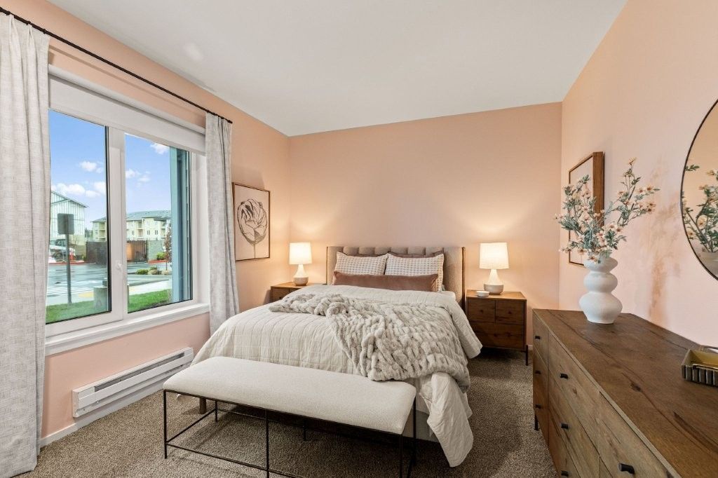 A bedroom with a bed , dresser , mirror and window.