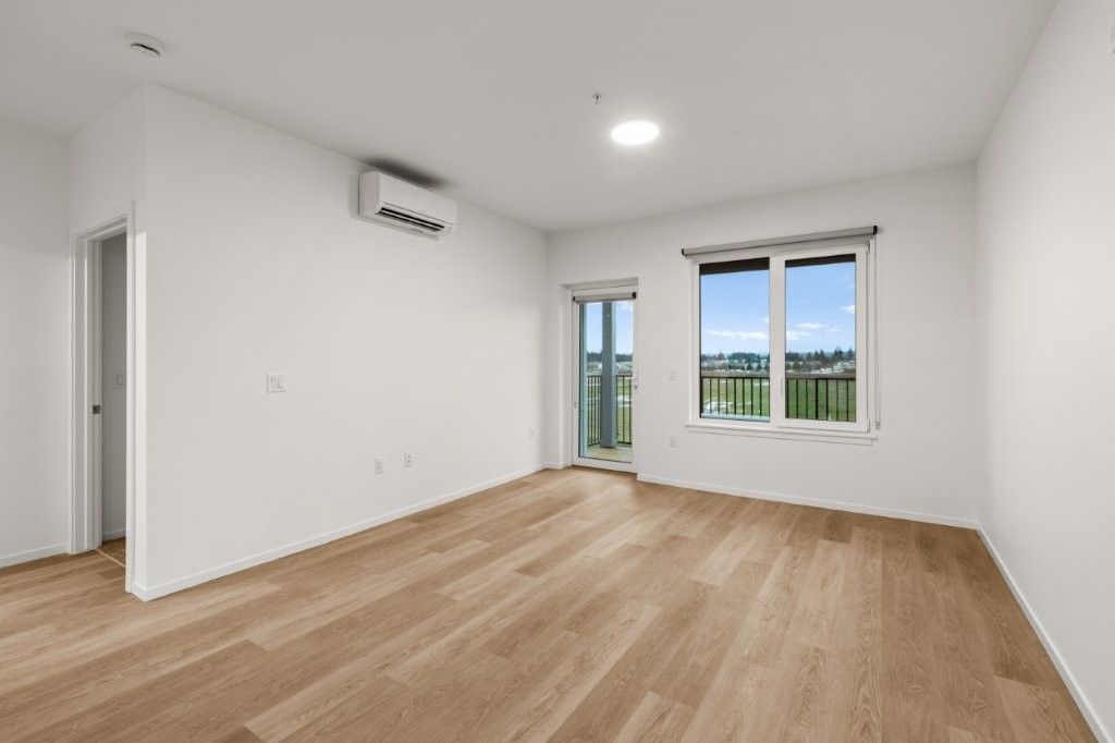 An empty living room with hardwood floors and white walls.
