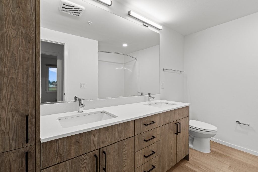 A bathroom with two sinks , a toilet , and a large mirror.