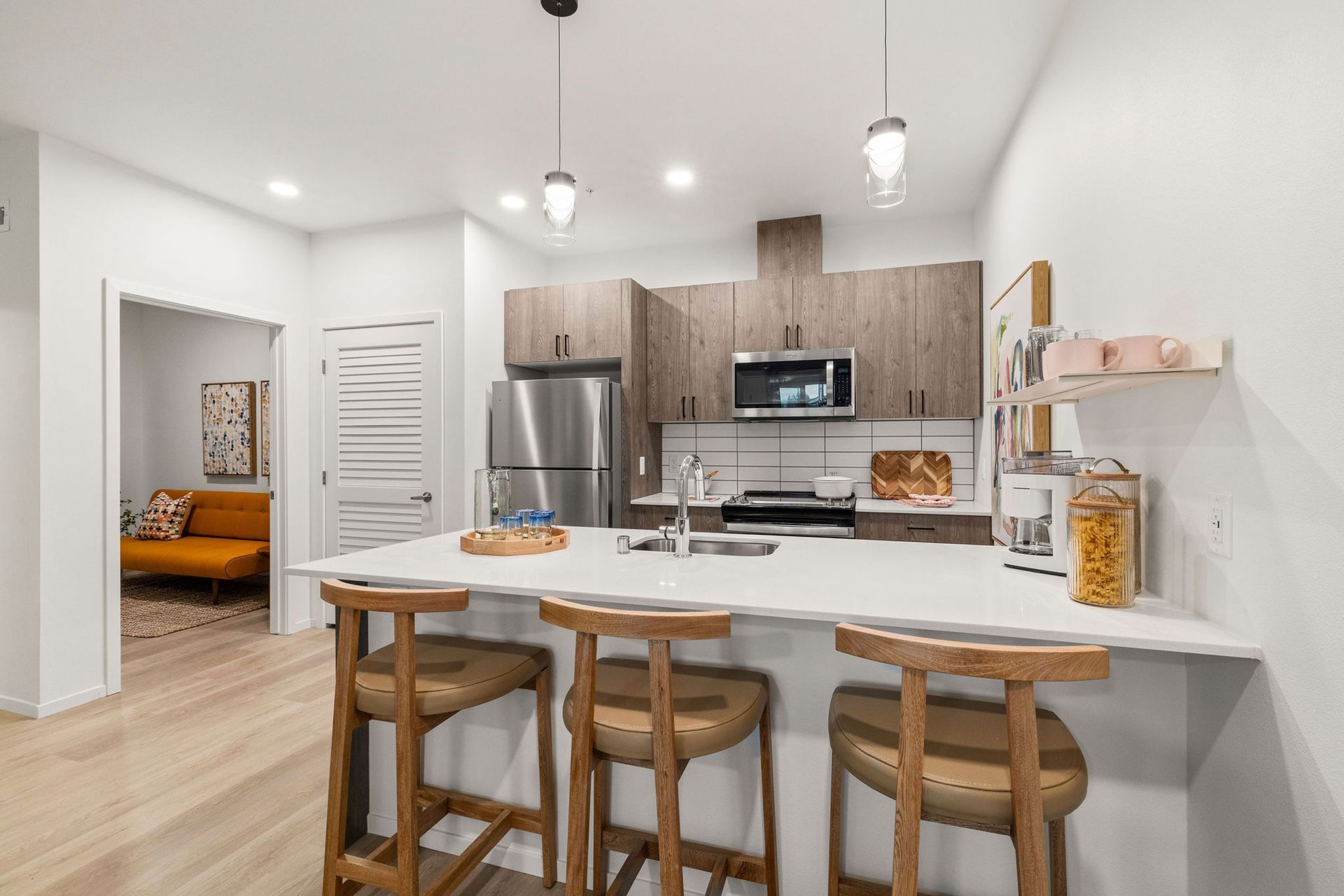 A kitchen with a large island , stools , a refrigerator and a microwave.
