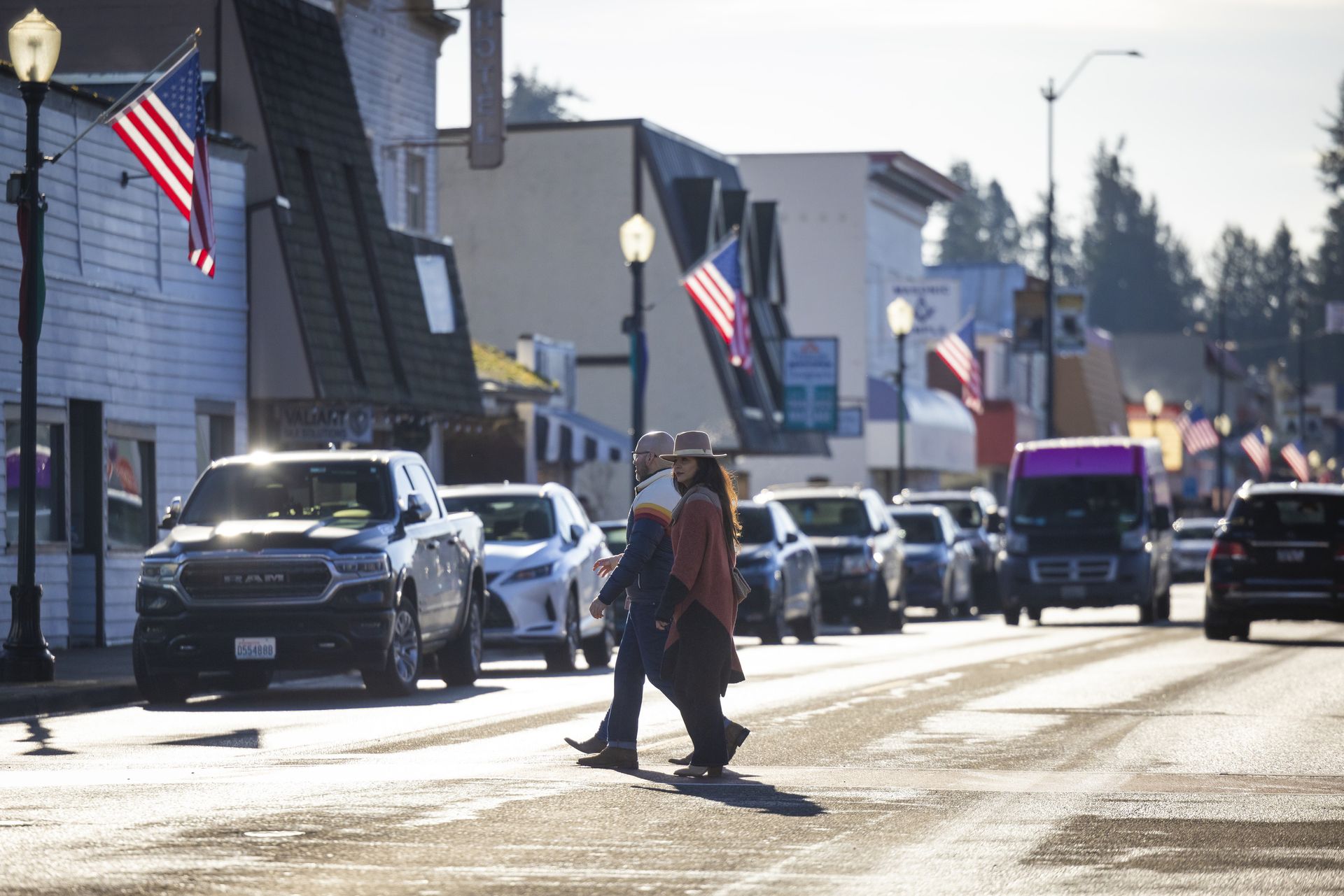 A couple of people are crossing a street in a small town.