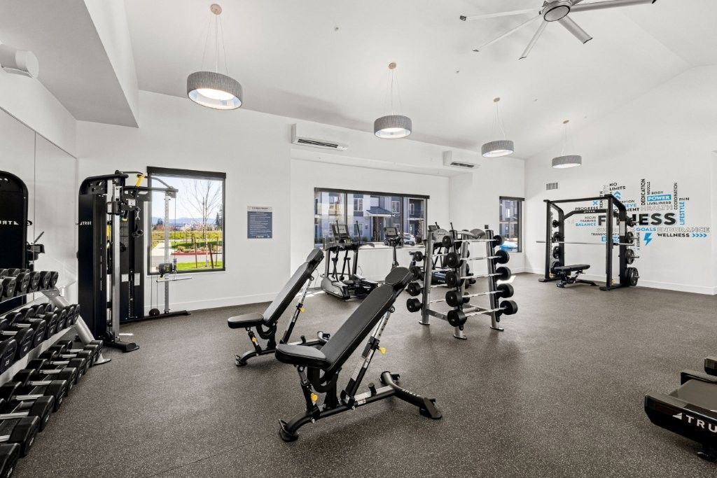 A large gym with a lot of exercise equipment and a ceiling fan.