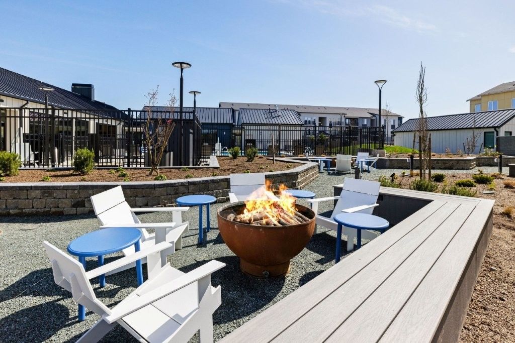 A fire pit is surrounded by chairs and tables in a patio area.