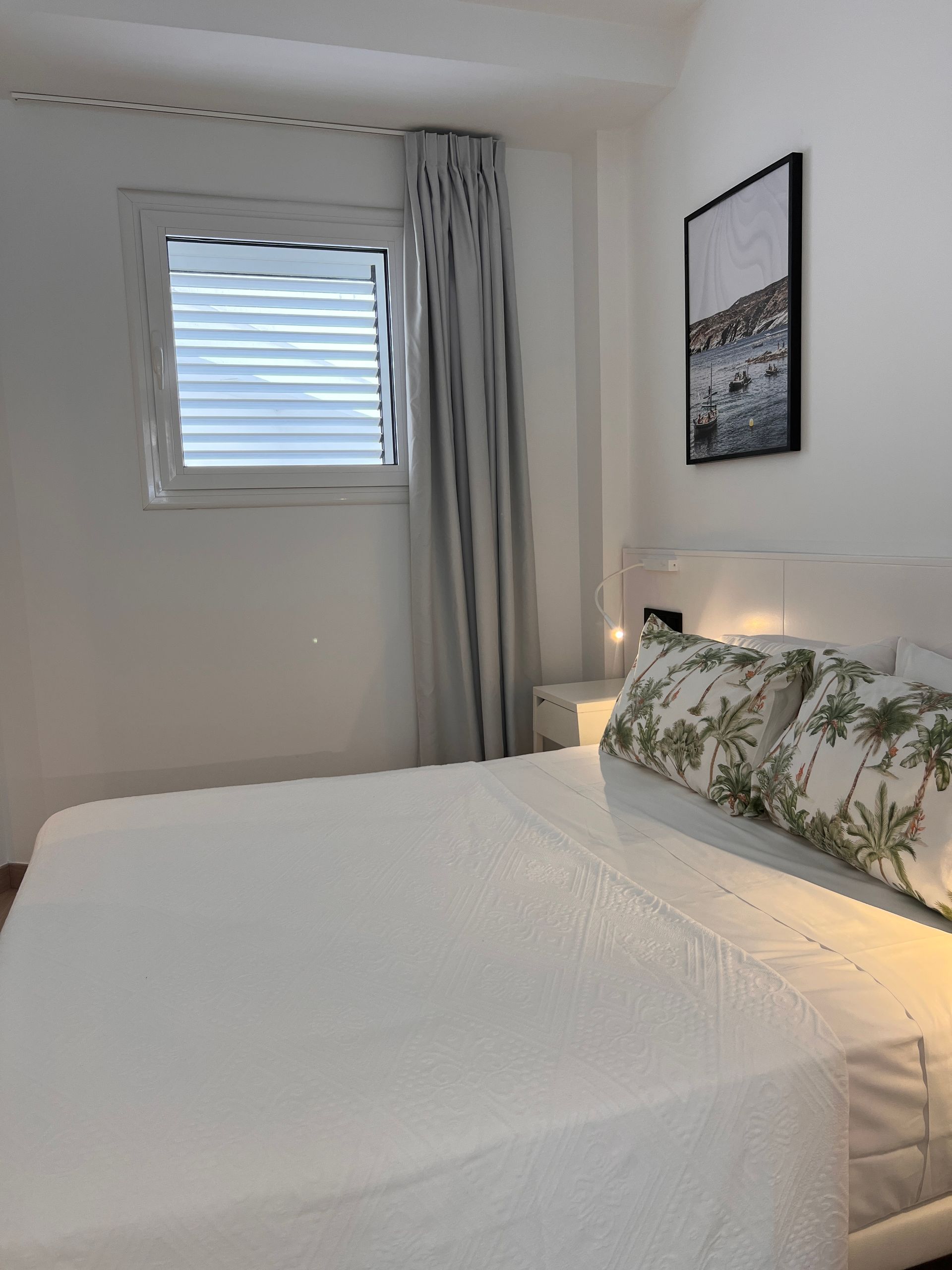 Bedroom with a white bed, window with blinds, gray curtains, and a framed art piece.