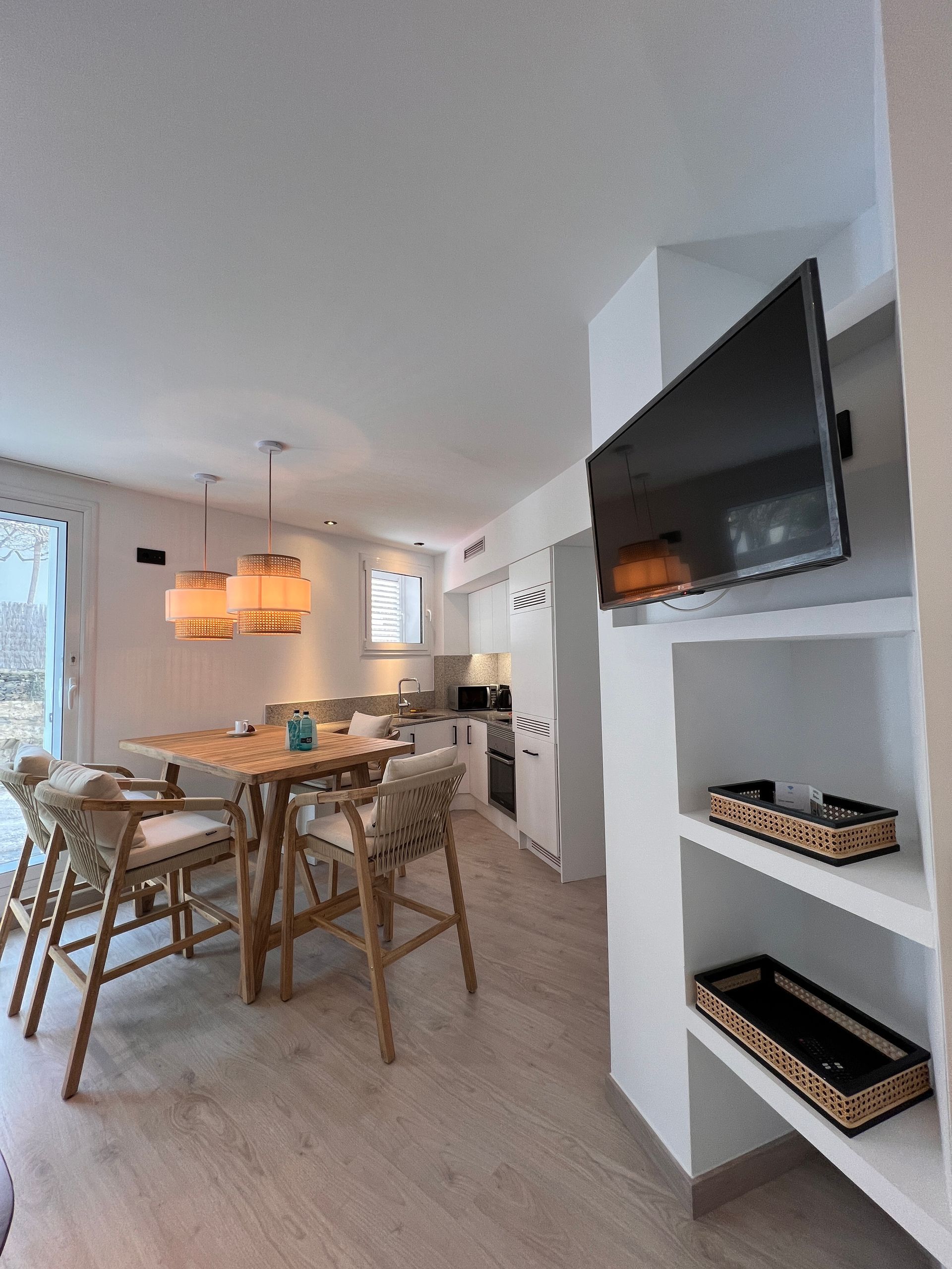 Modern kitchen and dining area with light wood furniture, white cabinetry, and a wall-mounted TV.