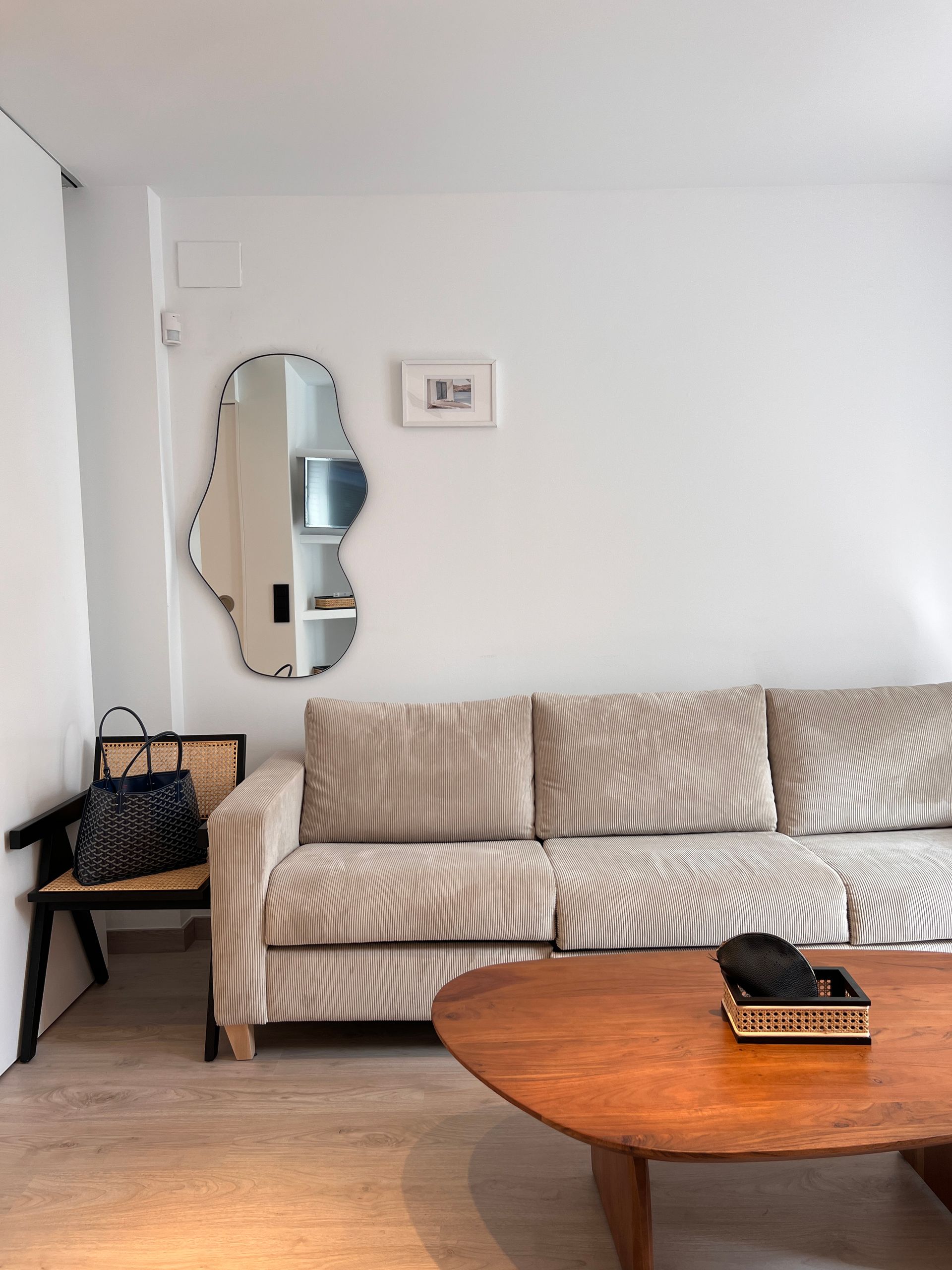 Living room with a sofa, unique mirror, and wooden table against a white wall.