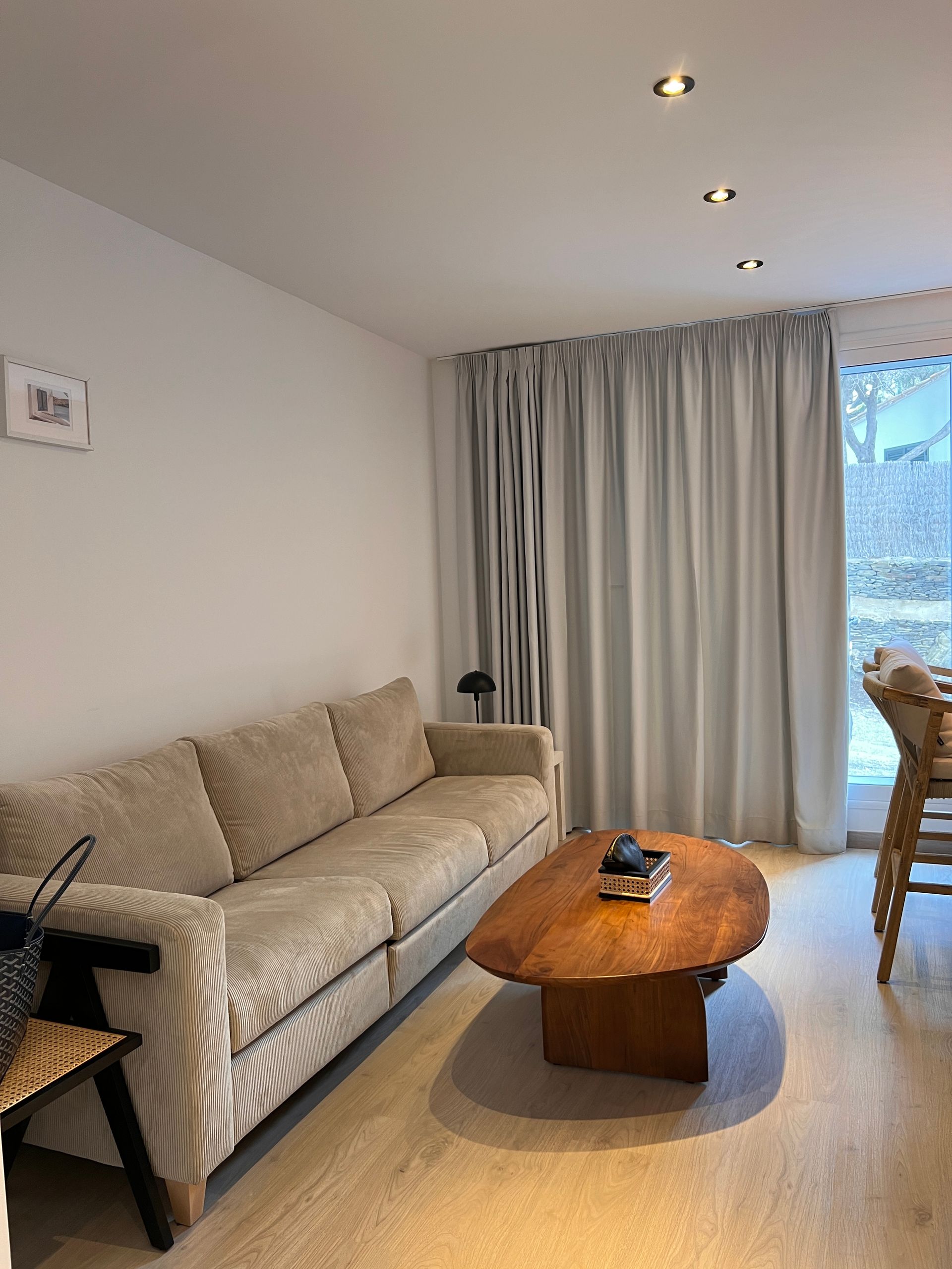 Living room with beige sofa, wooden coffee table, grey curtains, and wood chair.