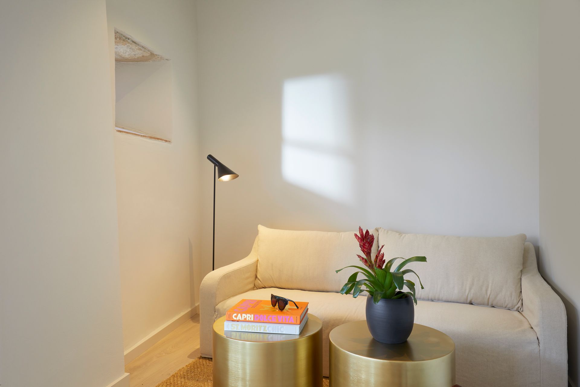 A living room with a couch , two tables , a lamp and a vase of flowers.