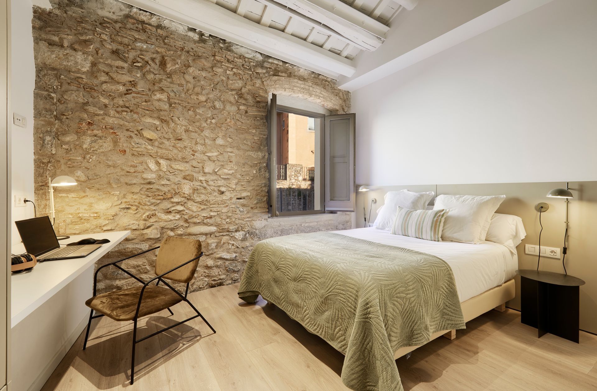 A bedroom with a large bed and a desk with a laptop on it.