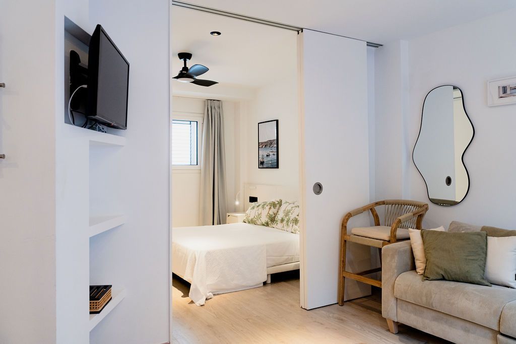 White-walled apartment interior with open pocket door revealing a bed. A TV and mirror are visible.