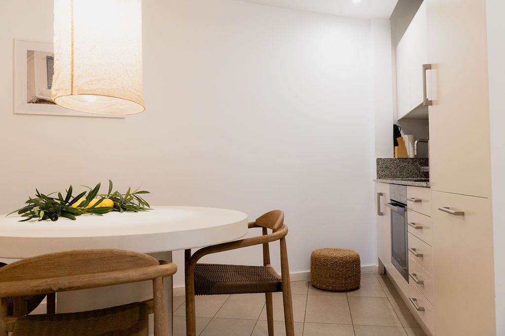 Bright, minimalist kitchen with round table, wooden chairs, and built-in appliances.
