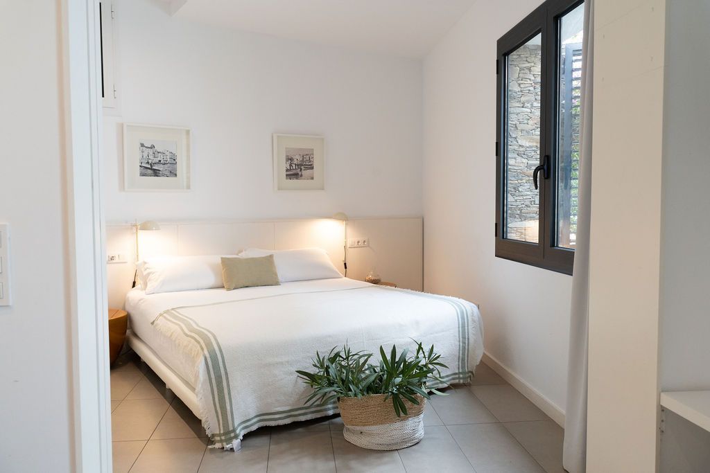 Bedroom with a bed, white walls, two framed prints, and a window.