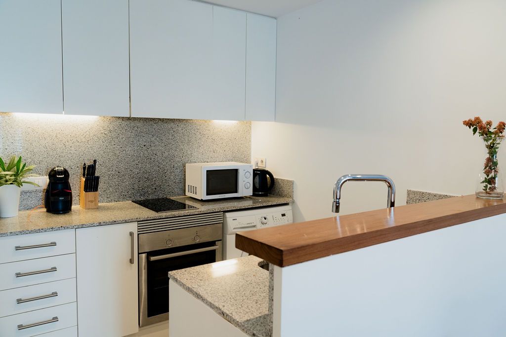 Modern white kitchen with granite countertops, stainless steel appliances, and a wooden bar.