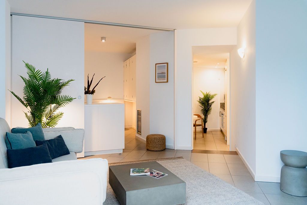 Modern living room with white walls, a sofa, and open doorways to other rooms.