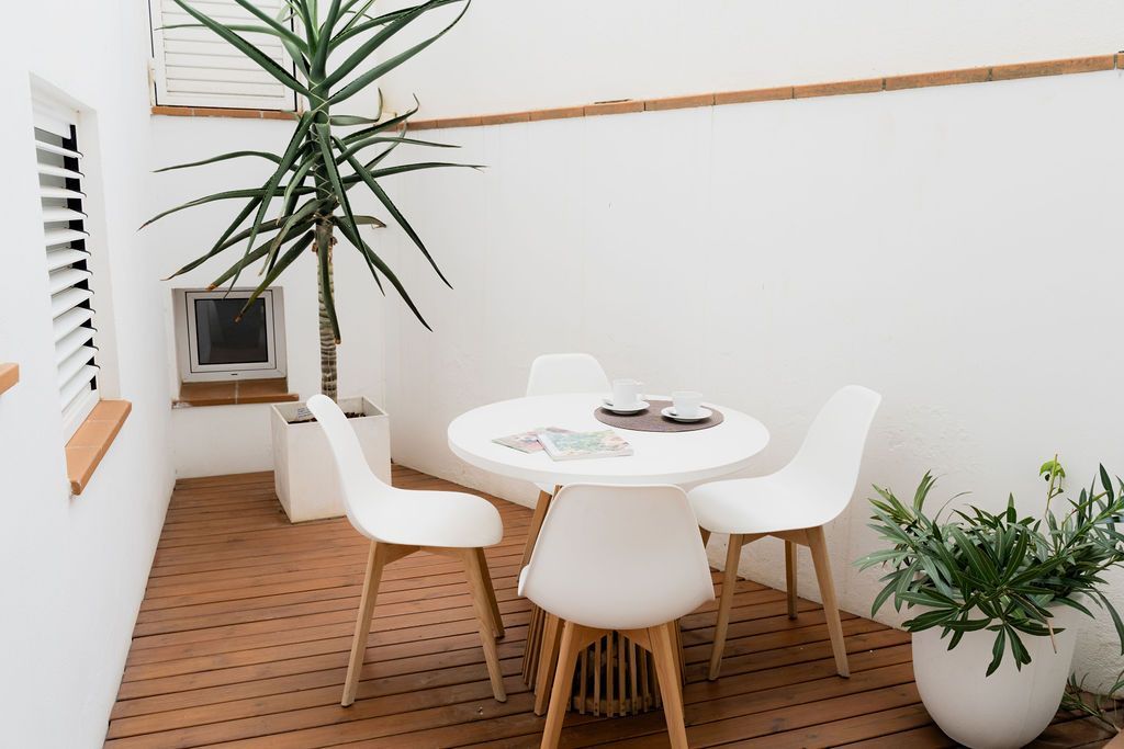White outdoor dining set with plant and wooden deck.