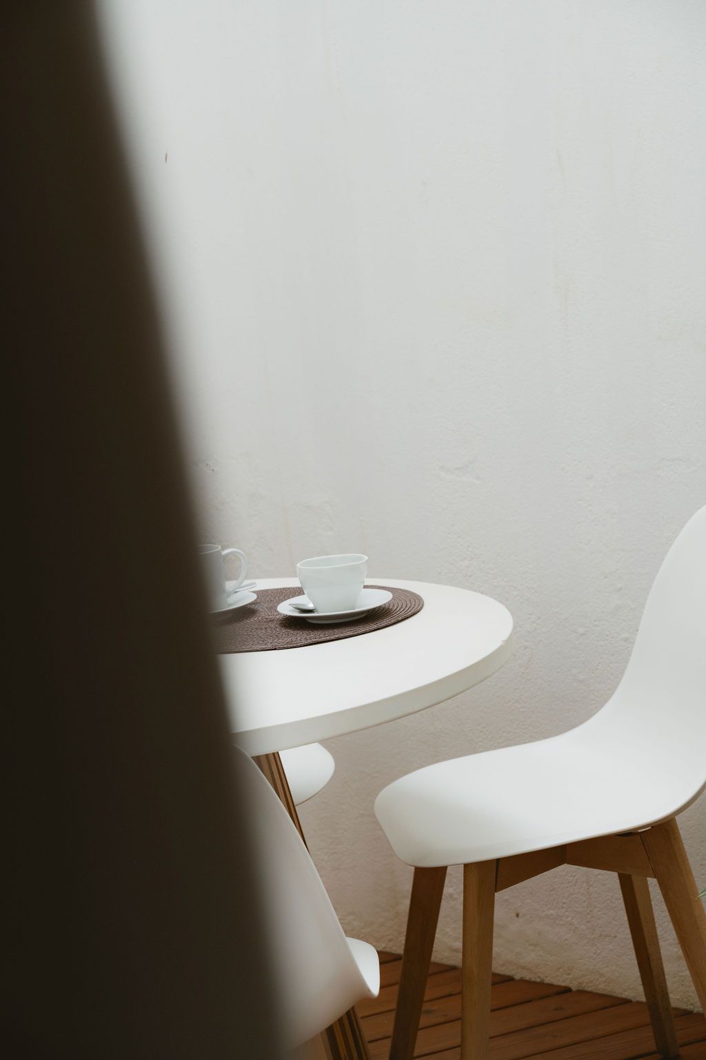 White table and chairs on a patio with a cup and saucer, set against a white wall.
