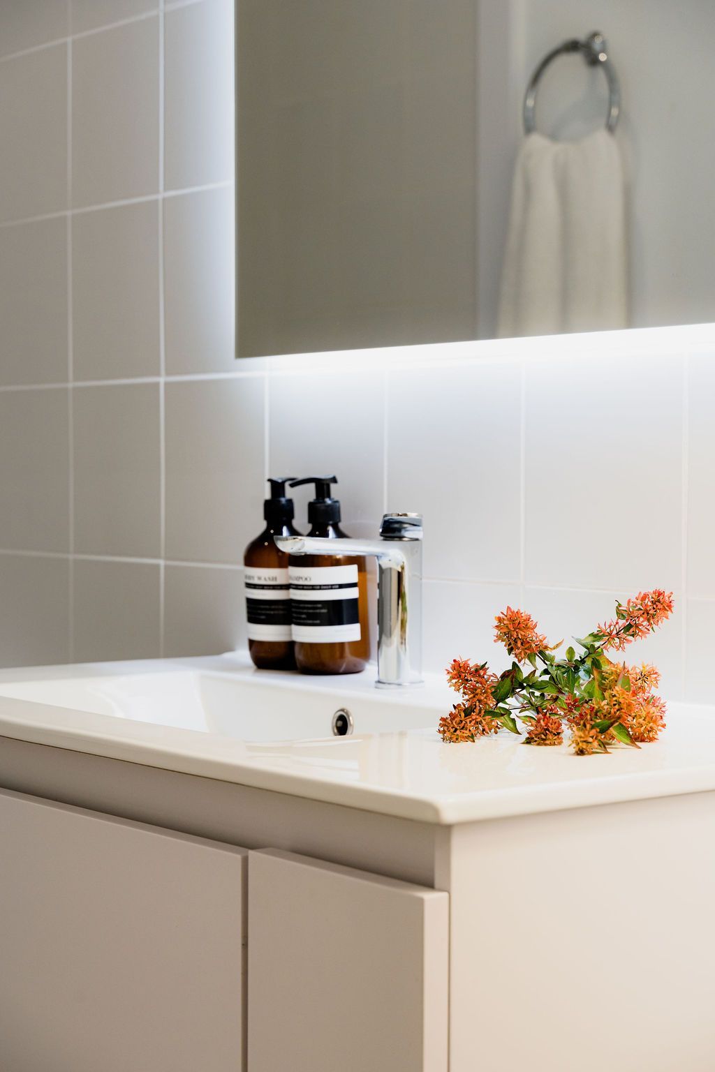 Bathroom sink with brown soap dispensers, flowers, and a mirror.