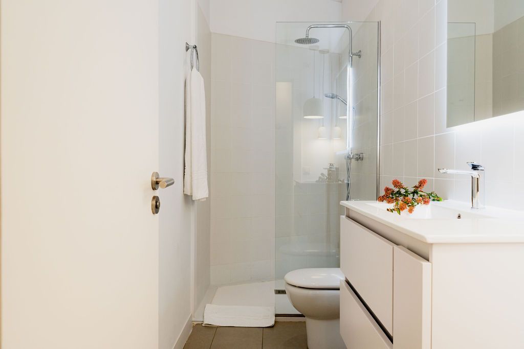White bathroom with a shower, toilet, and vanity. A towel hangs on the wall.