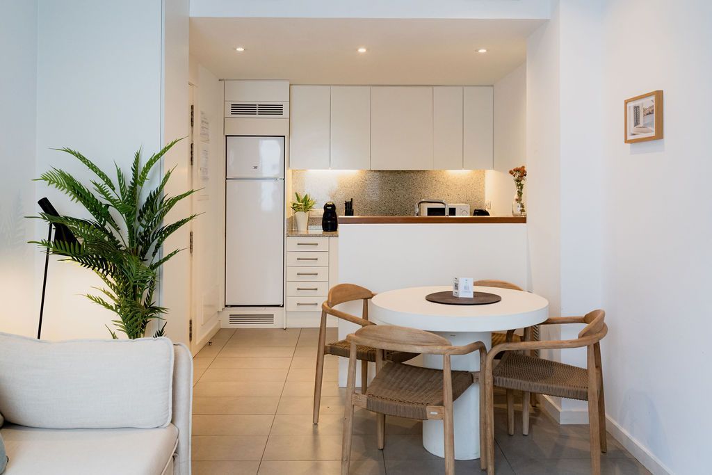 Small, bright kitchen with a round table and chairs. White cabinets and fridge, plant in the corner.