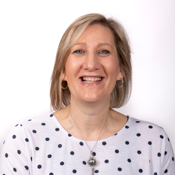 A woman wearing a polka dot shirt and a necklace is smiling.