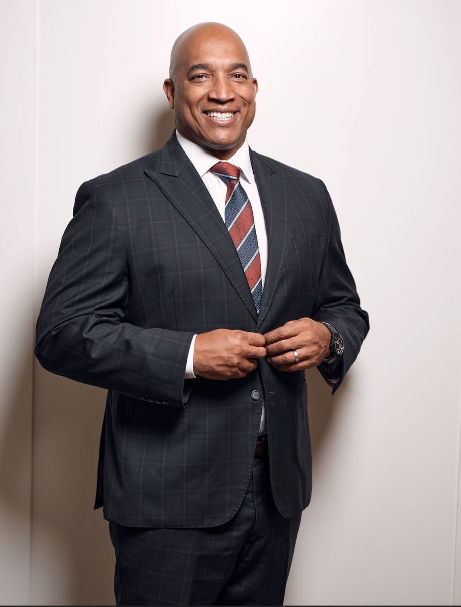 A man in a suit and tie is standing in front of a white wall.