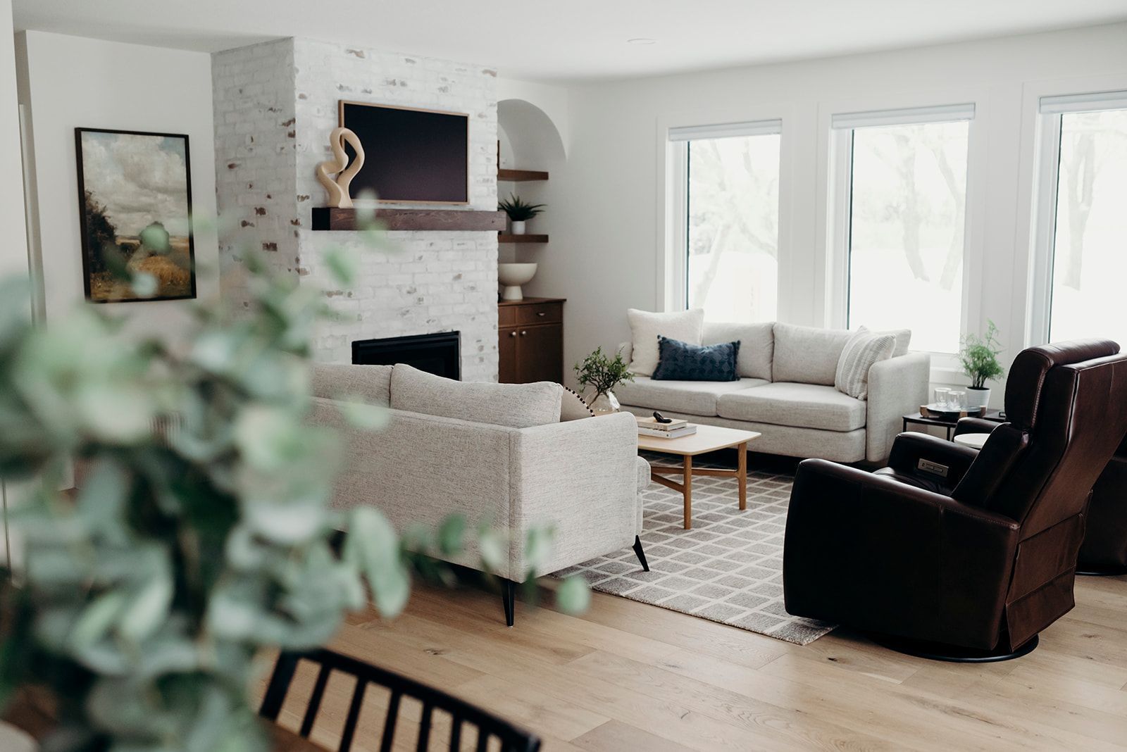Living room with a fireplace, sofas, and windows. White walls, wooden floors, and modern decor.