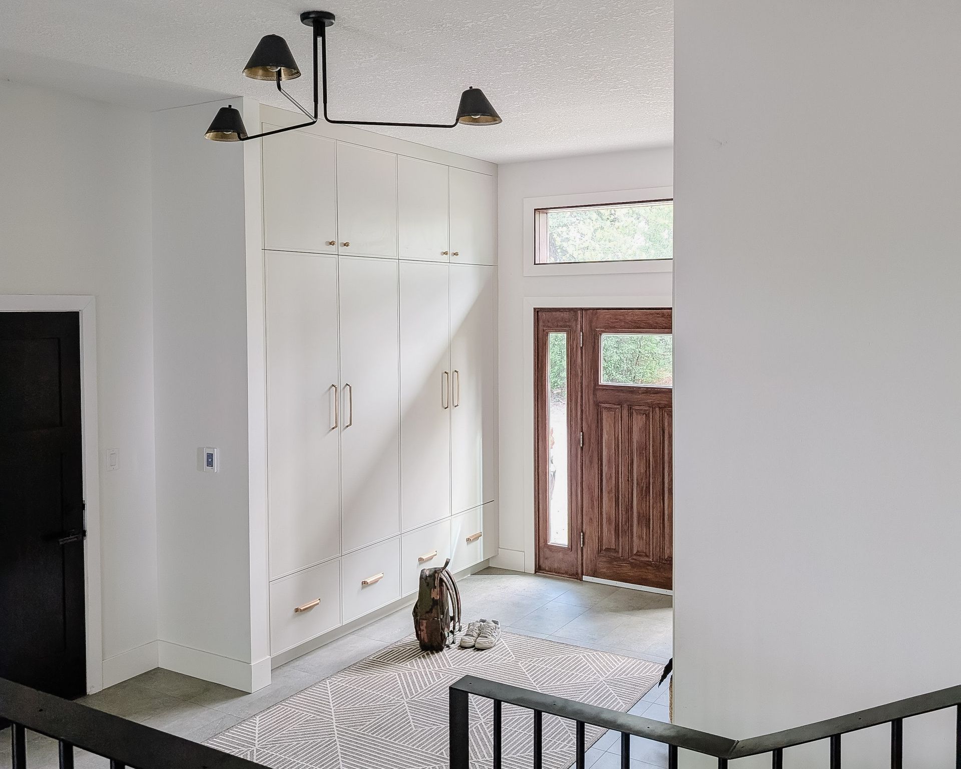 Entryway with white storage cabinets, wood door, overhead light fixture, and rug.