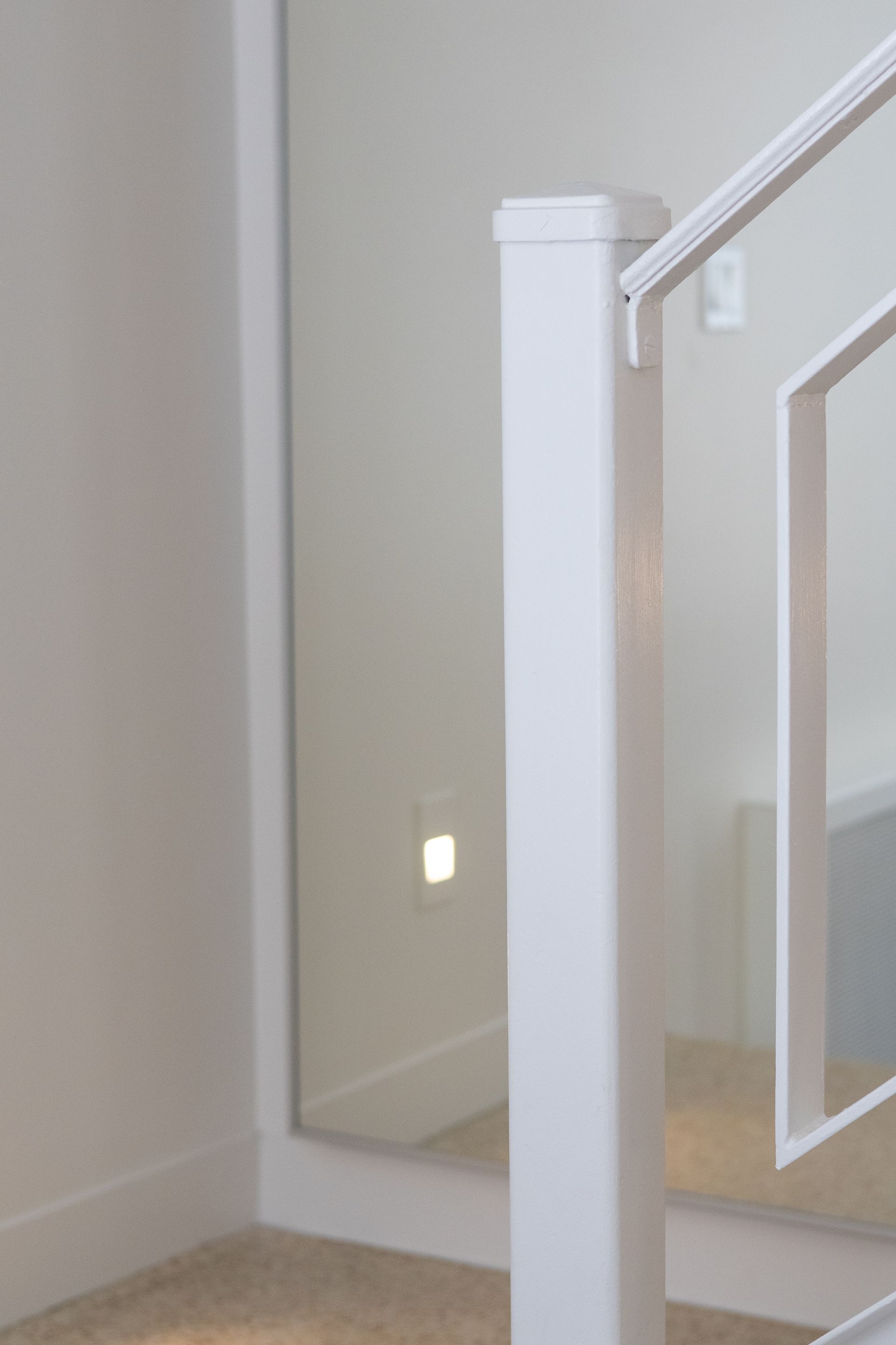 Poteau de rampe d'escalier blanc et balustres géométriques à côté d'un mur en miroir avec une seule prise éclairée.