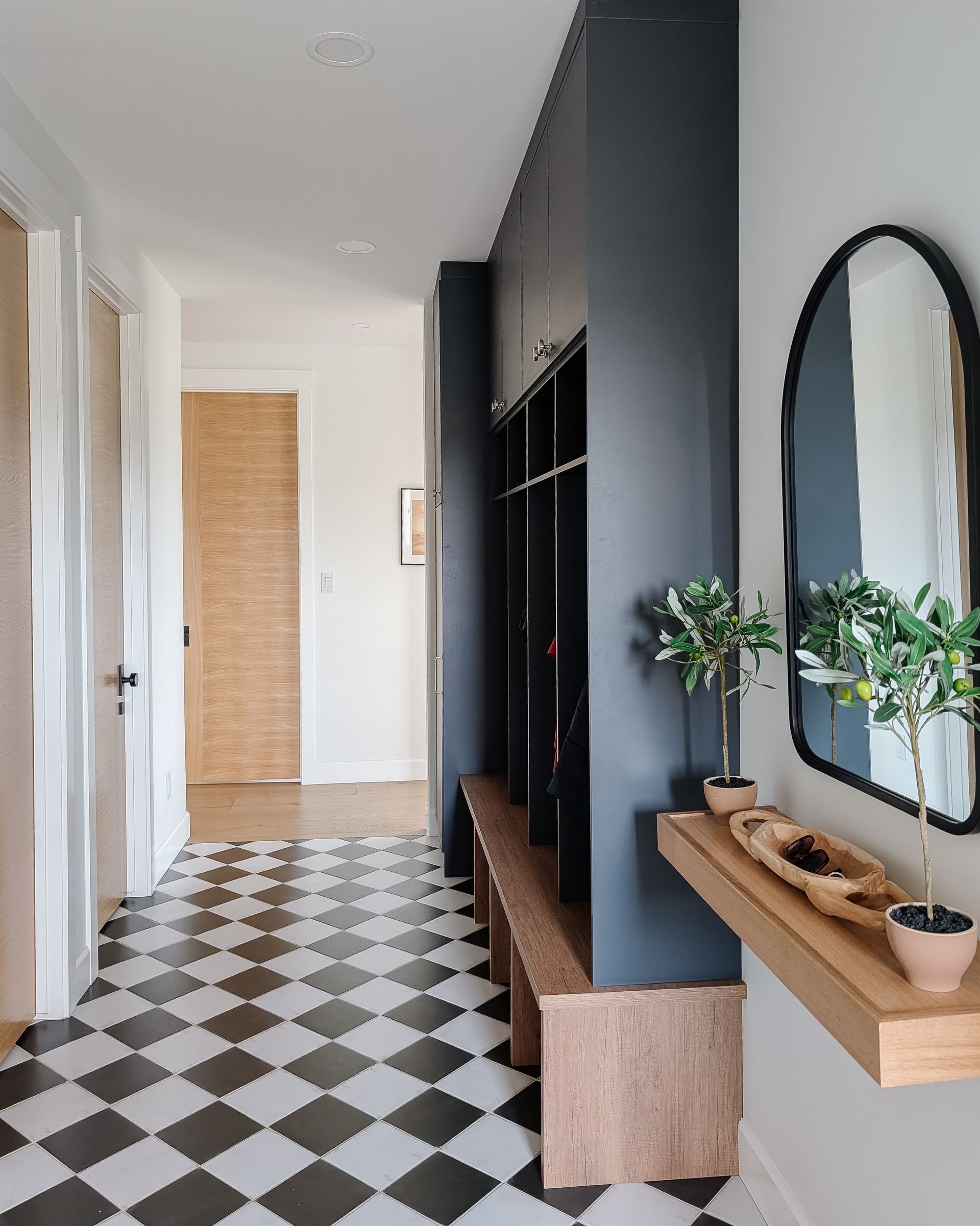 A narrow closet or mudroom with black shelving units holding gray storage containers and folded clothing. A blue jacket hangs