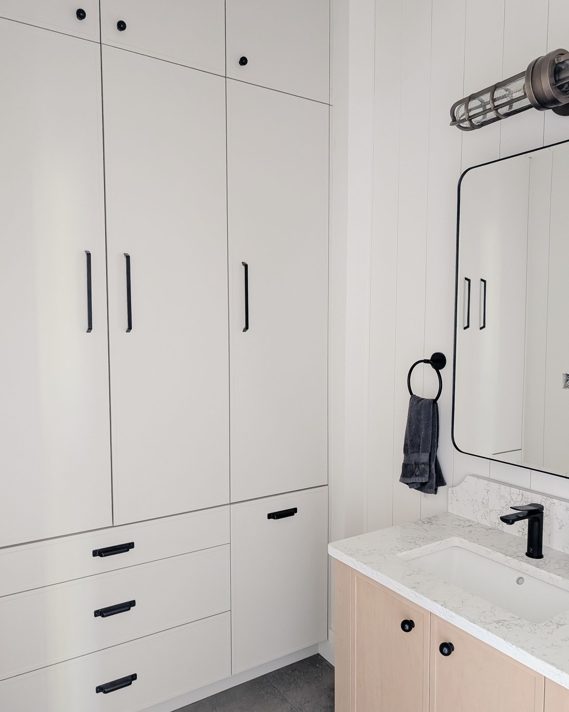 White bathroom with tall cabinets, a vanity, mirror, and black hardware.