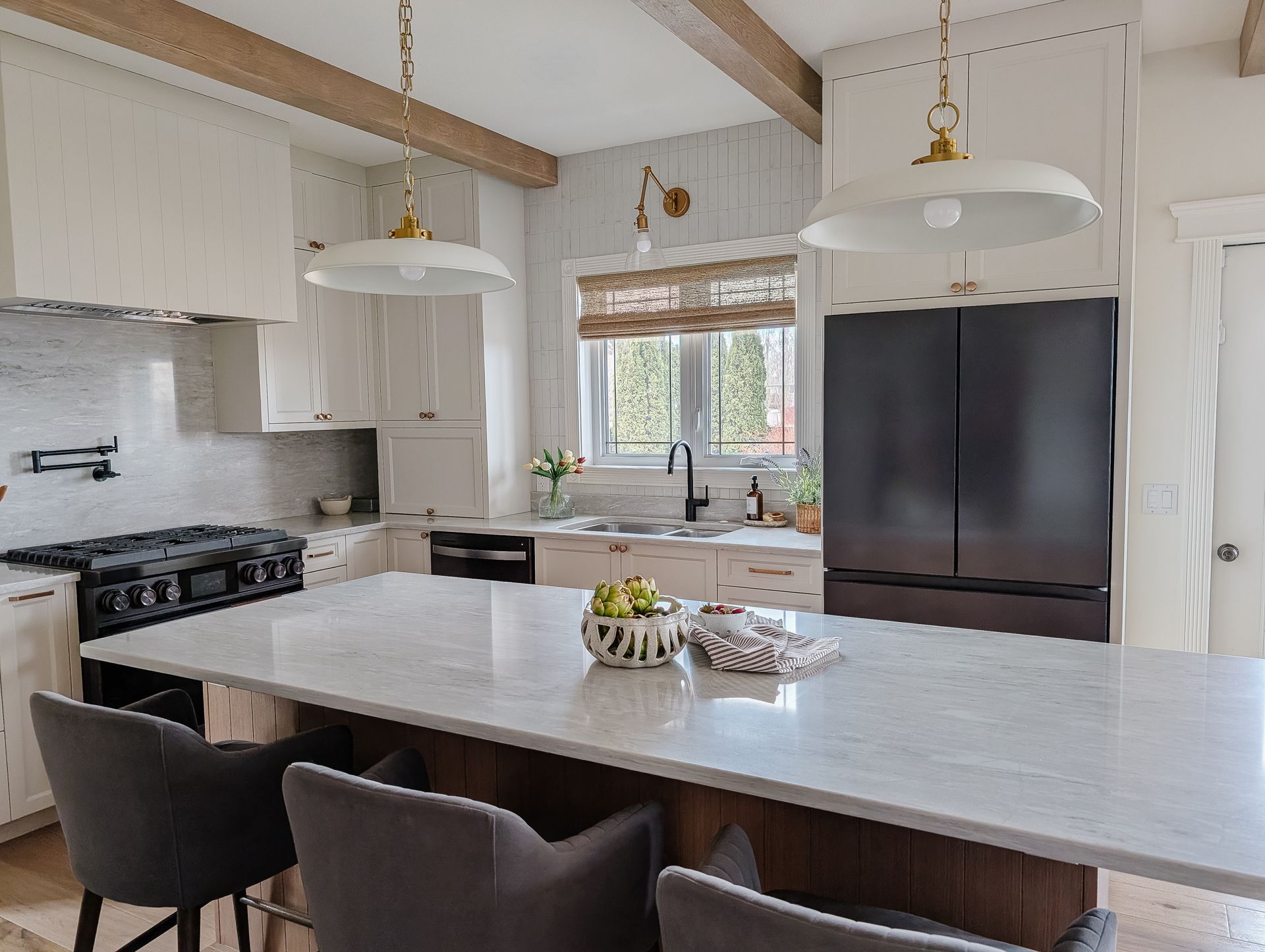 Modern kitchen with white cabinets, dark appliances, marble countertops, and island with gray stools.