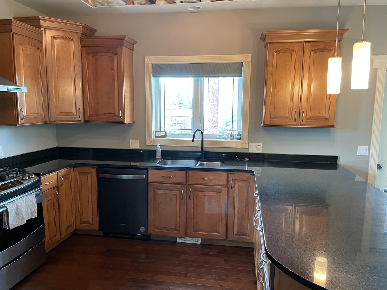 Kitchen with light brown cabinets, dark countertops, a window, and a black sink.