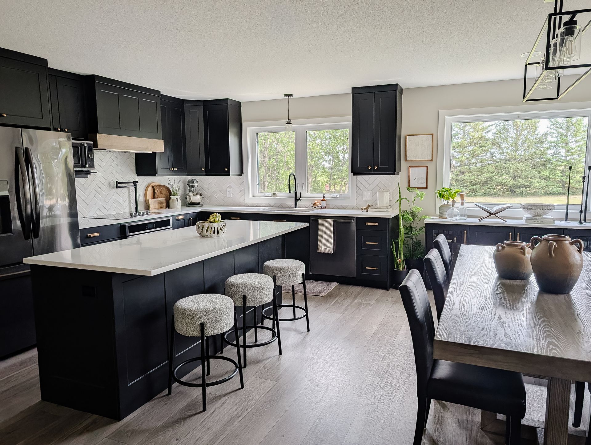 Modern black and white kitchen with island, stools, stainless steel appliances, and dining table.