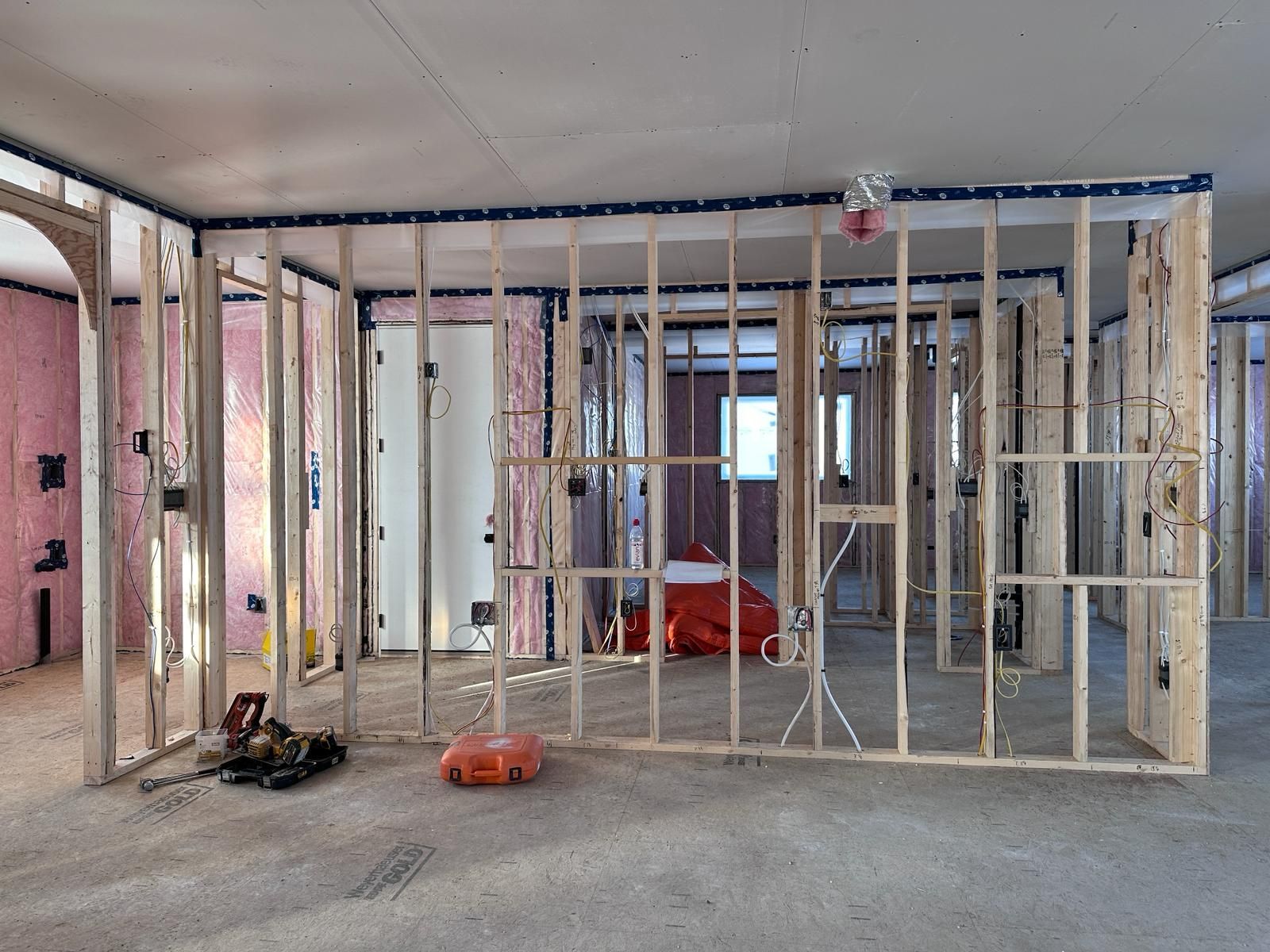 Interior of a building under construction, framed walls with pink insulation visible, concrete floor.